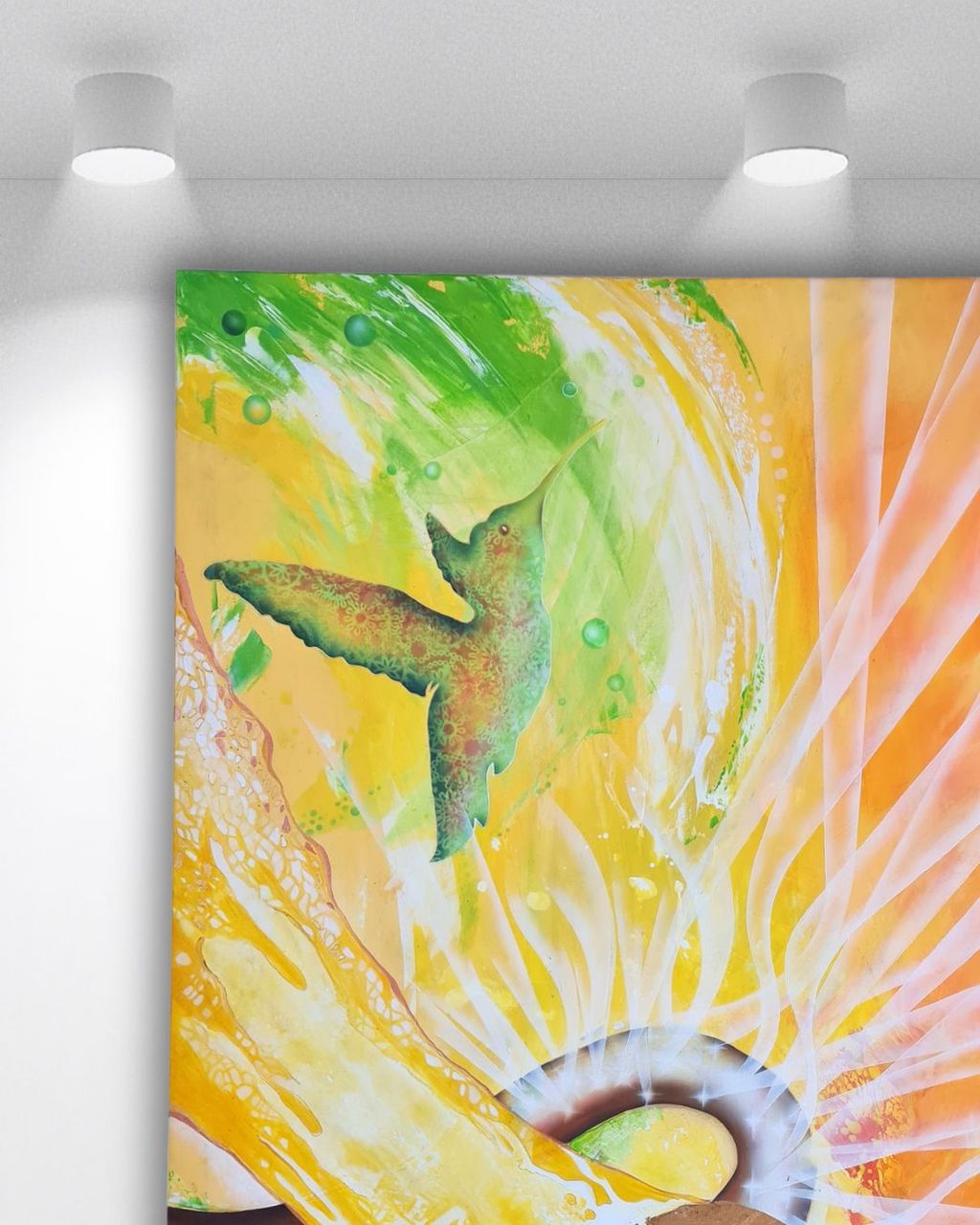 Bunte Wandmalerei mit einem grünen Kolibri vor einem gelben und orangefarbenen Hintergrund mit abstrahierten Lichtstrahlen und Mustern.